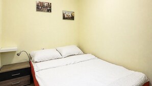Ein Einzelbett mit weißer Bettwäsche in einem Zimmer mit hellgelben Wänden, einem Nachttisch und zwei kleinen Bildern an der Wand.