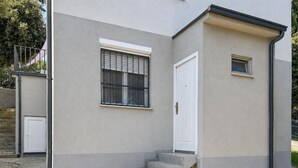 Ein Gebäude mit einer grauen Fassade, einer weißen Tür und einem kleinen Fenster.