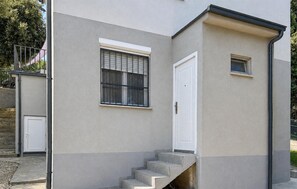 Ein Gebäude mit einer grauen Fassade, einer weißen Tür und einem kleinen Fenster.