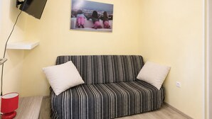 Ein Zimmer mit einer Couch, einem Wand-Fernseher, einer roten Lampe und einem gerahmten Bild an der Wand.