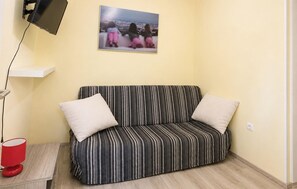 Ein Zimmer mit einer Couch, einem Wand-Fernseher, einer roten Lampe und einem gerahmten Bild an der Wand.