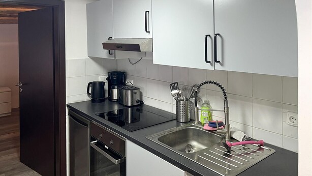 Een moderne keuken met een zwart aanrecht, roestvrijstalen apparatuur, een koffiezetapparaat en een spoelbak met een kraan.