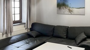 Een moderne woonkamer met een zwarte leren bank, een witte salontafel en een raam met gordijnen.