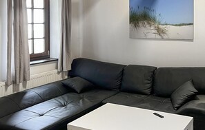 A modern living room with a black leather sofa, a white coffee table, and a window with curtains. - Lovely apartment in Kalkhorst with WiFi (Kalkhorst)