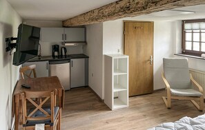 A compact room with a kitchenette, a wooden door, a white shelving unit, a cushioned chair, and a bed. - 1 bedroom stunning apartment in Kalkhorst (Kalkhorst)