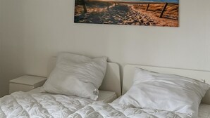 Een bed met een gewatteerde witte deken, twee witte kussens en een nachtkastje met een witte lamp.
