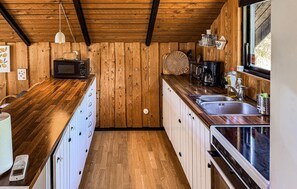 A compact kitchen with wooden walls, a microwave, a coffee maker, and a sink. - Amazing home in Rødby with WiFi (Rødby)
