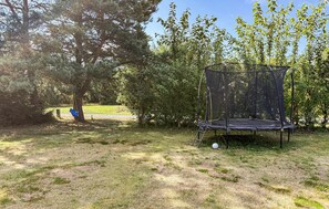 A trampoline set up in a grassy area with a swing set and trees in the background. - Amazing home in Rødby with WiFi (Rødby)
