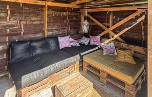 A rustic wooden cabin interior with a black leather sofa, cushioned bench, and decorative pillows. - Amazing home in Rødby with WiFi (Rødby)