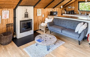 A cozy living room with a fireplace, a sofa, a coffee table, and a kitchen area with a microwave and coffee maker. - Amazing home in Rødby with WiFi (Rødby)