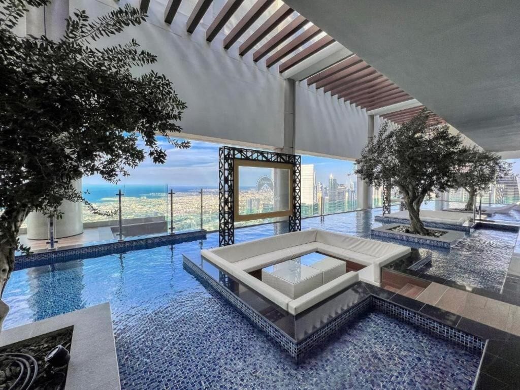 An indoor infinity pool with a view of a city skyline, a seating area, and a large tree.