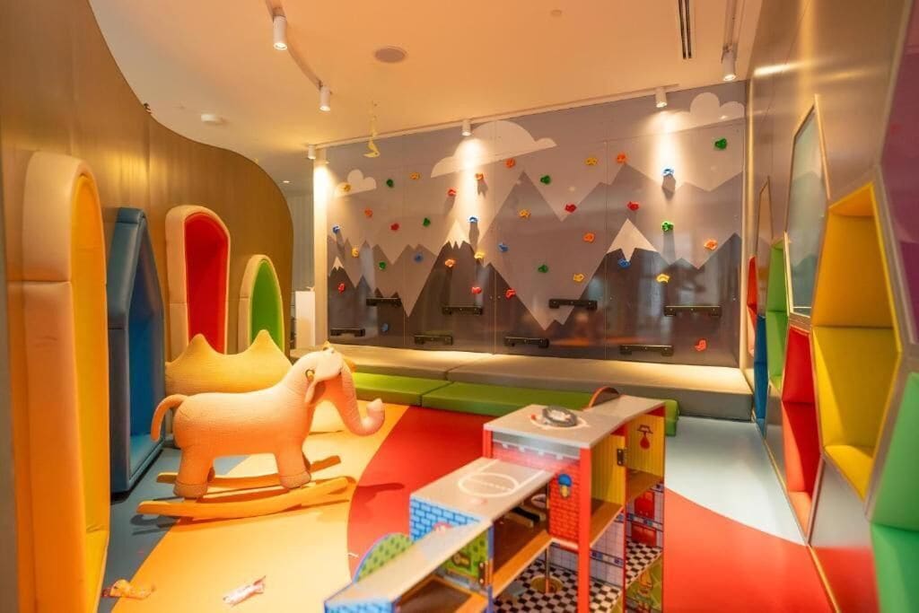 Un área de juegos infantiles con coloridas paredes de escalar, un caballo balancín y una mesa de juegos.