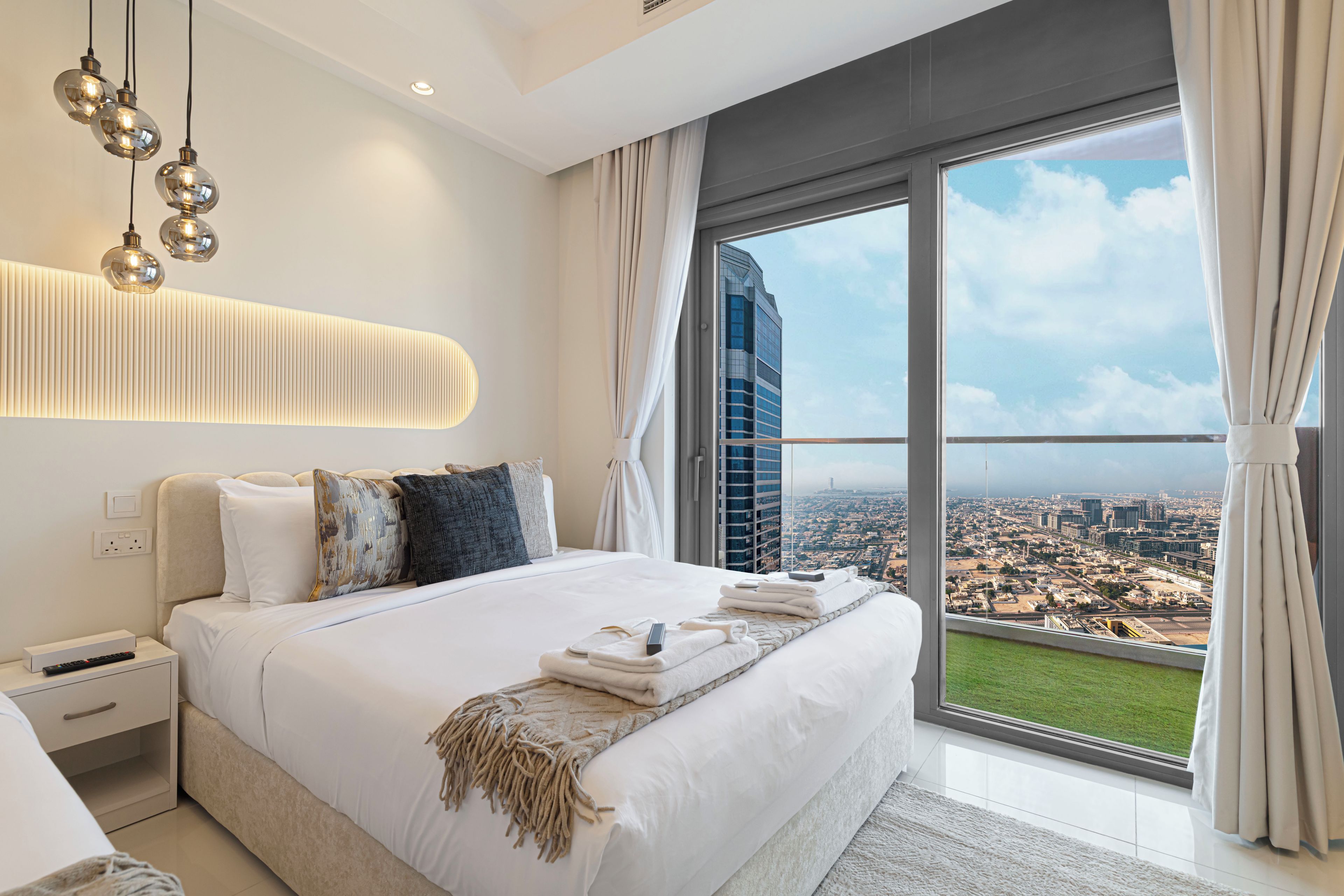 Quarto moderno com uma cama grande, vista da cidade e luminária de parede diferenciada.