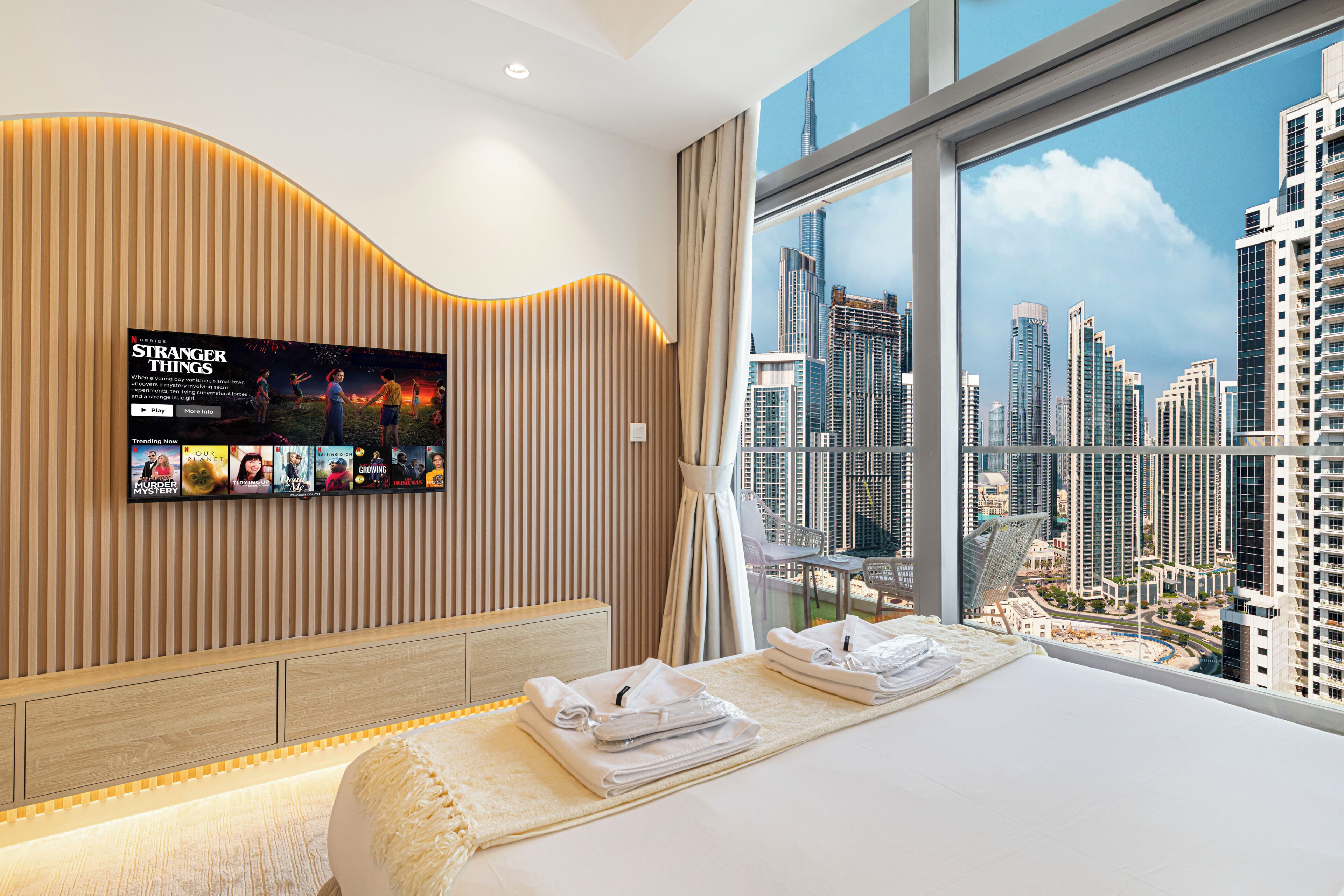 Quarto de hotel com uma cama grande, uma TV fixada na parede e vista para a paisagem urbana pela janela.