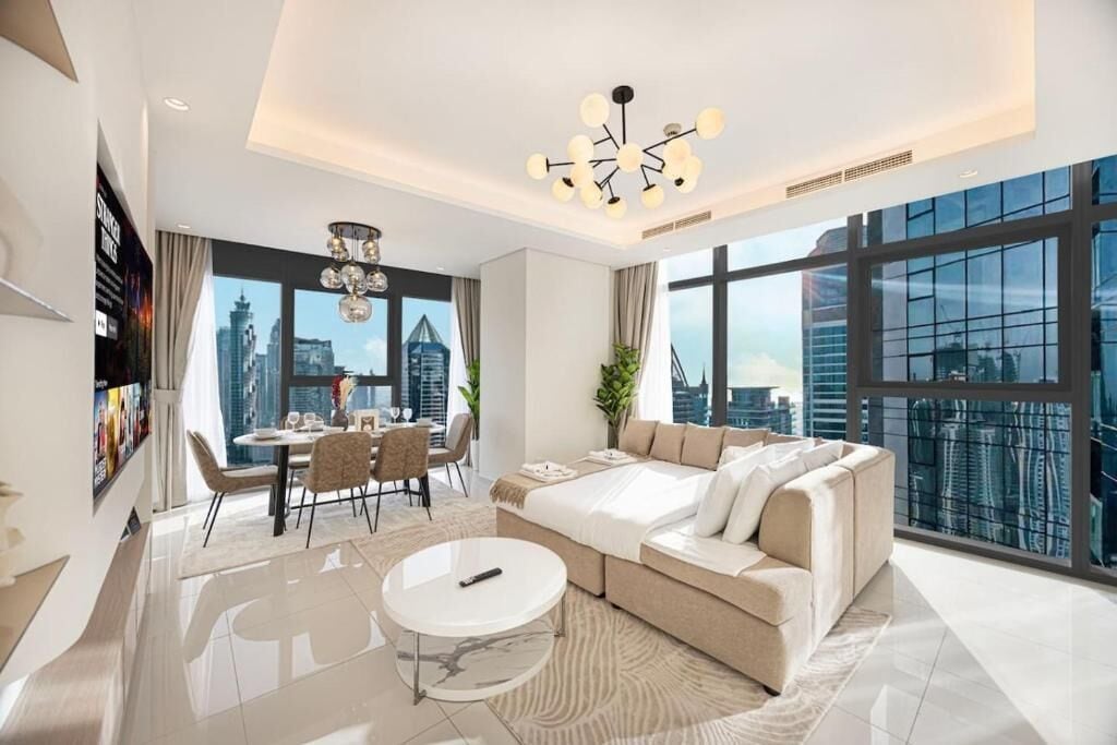 Uma sala de estar moderna com sofá, mesa de jantar e cadeiras, janelas amplas com vista para a cidade e um candelabro.