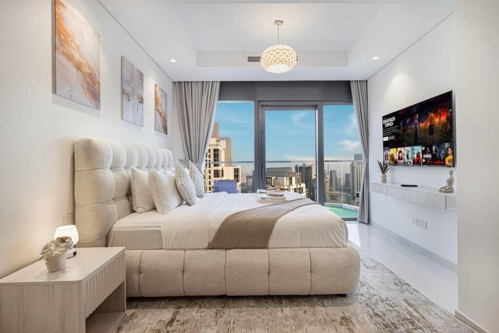 A modern bedroom with a large bed, a TV, and a city view.