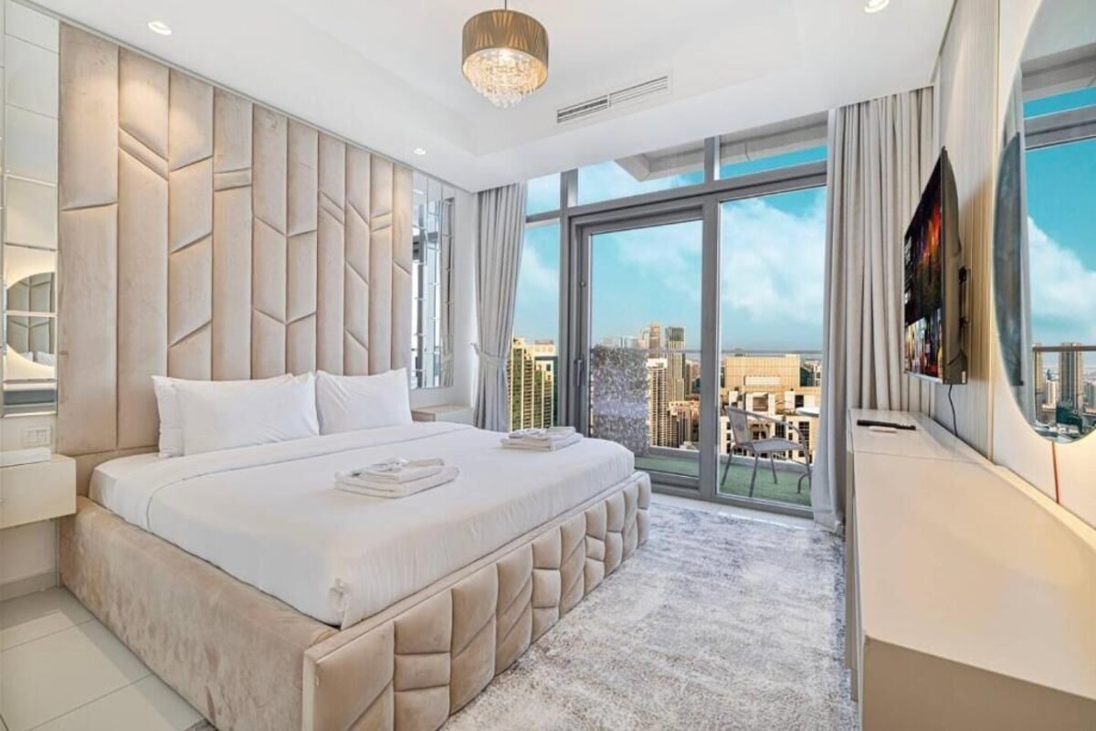 Ein modernes Schlafzimmer mit einem großen Bett, Blick auf die Stadt und einem Fernseher an der Wand.