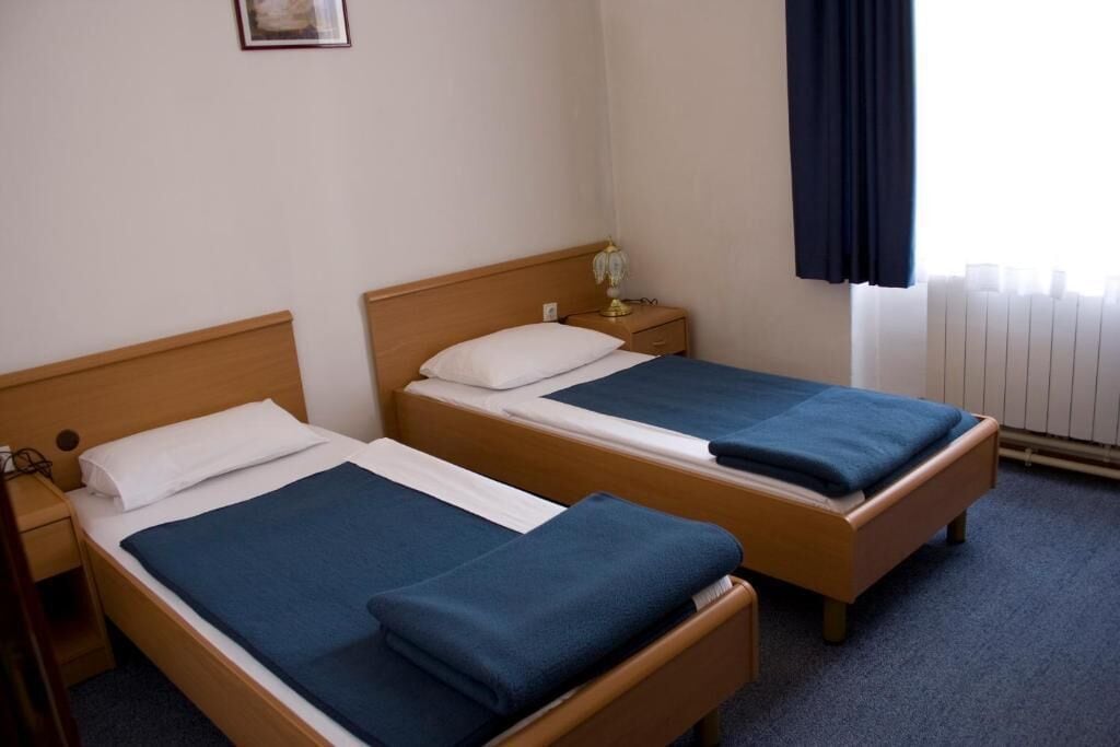 Hotellihuone, jossa on kaksi erillistä sänkyä, yöpöytä lampun kanssa ja ikkuna, jossa on verhot.