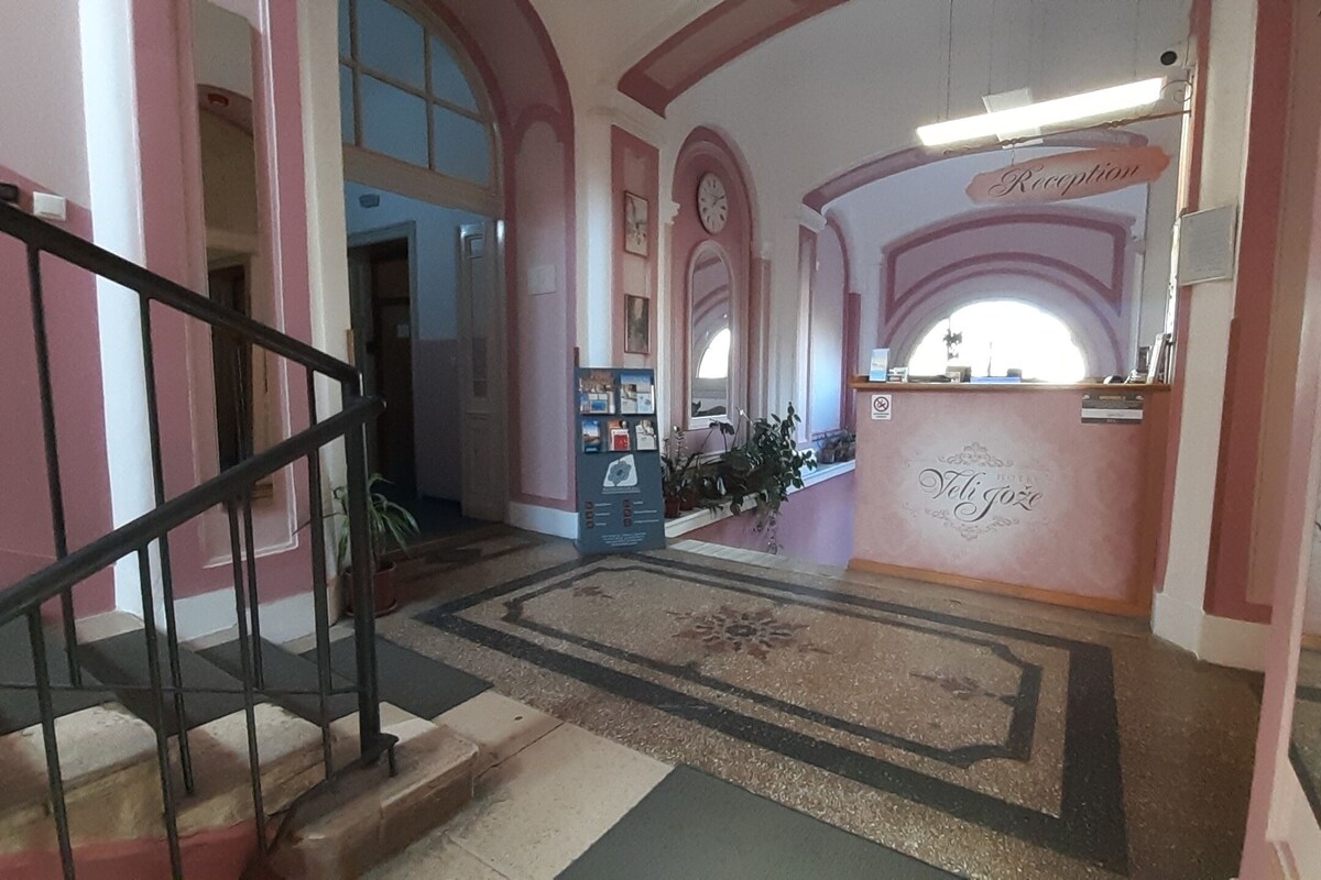 Zona de recepción de un hotel, con mostrador, una escalera y un reloj en la pared.