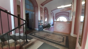 A hotel reception area with a reception desk, a staircase, and a wall with a clock.