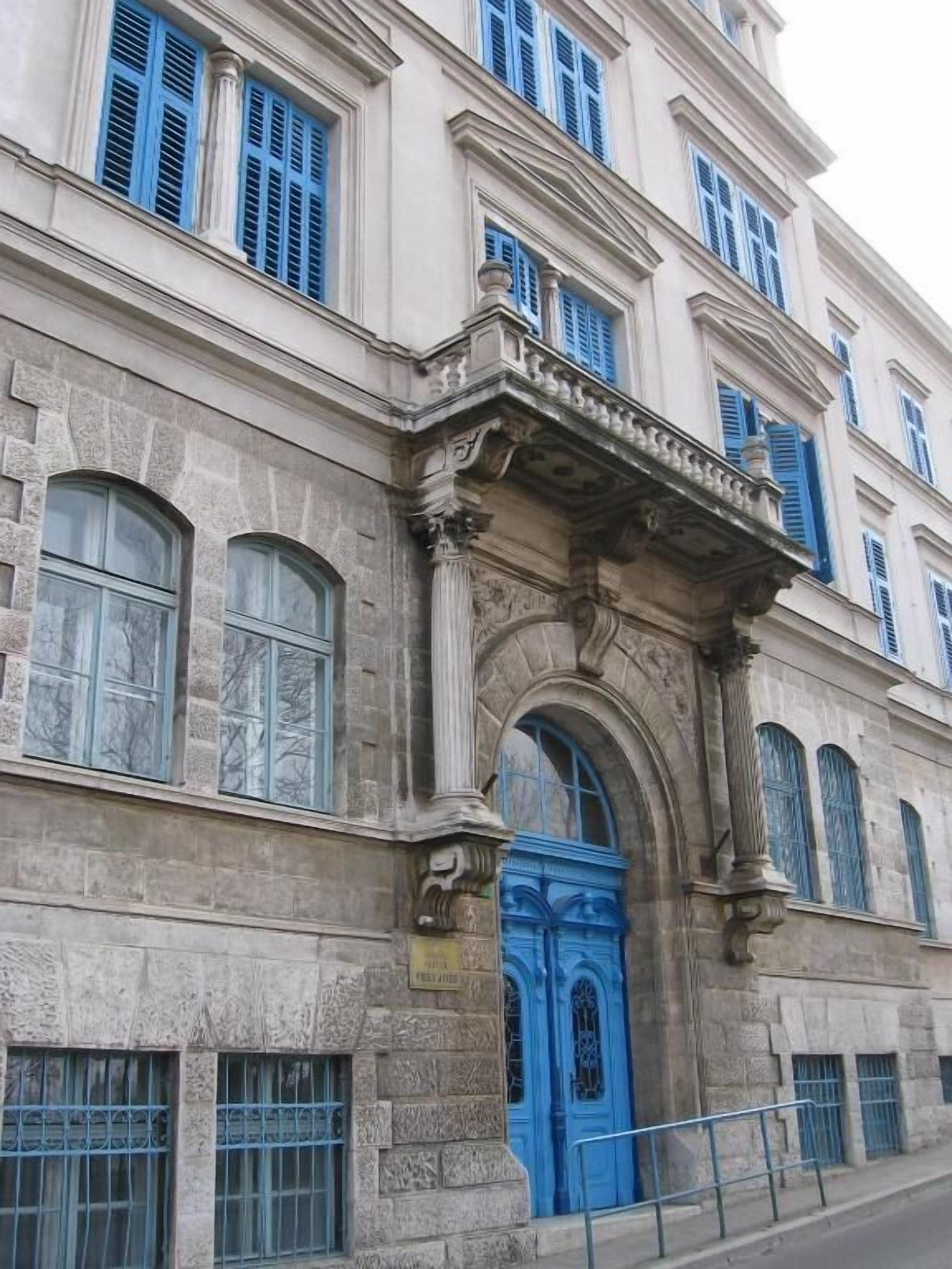 Ein historisches Gebäude mit einem markanten Bogenportal, großen Fenstern und einer blauen Tür.