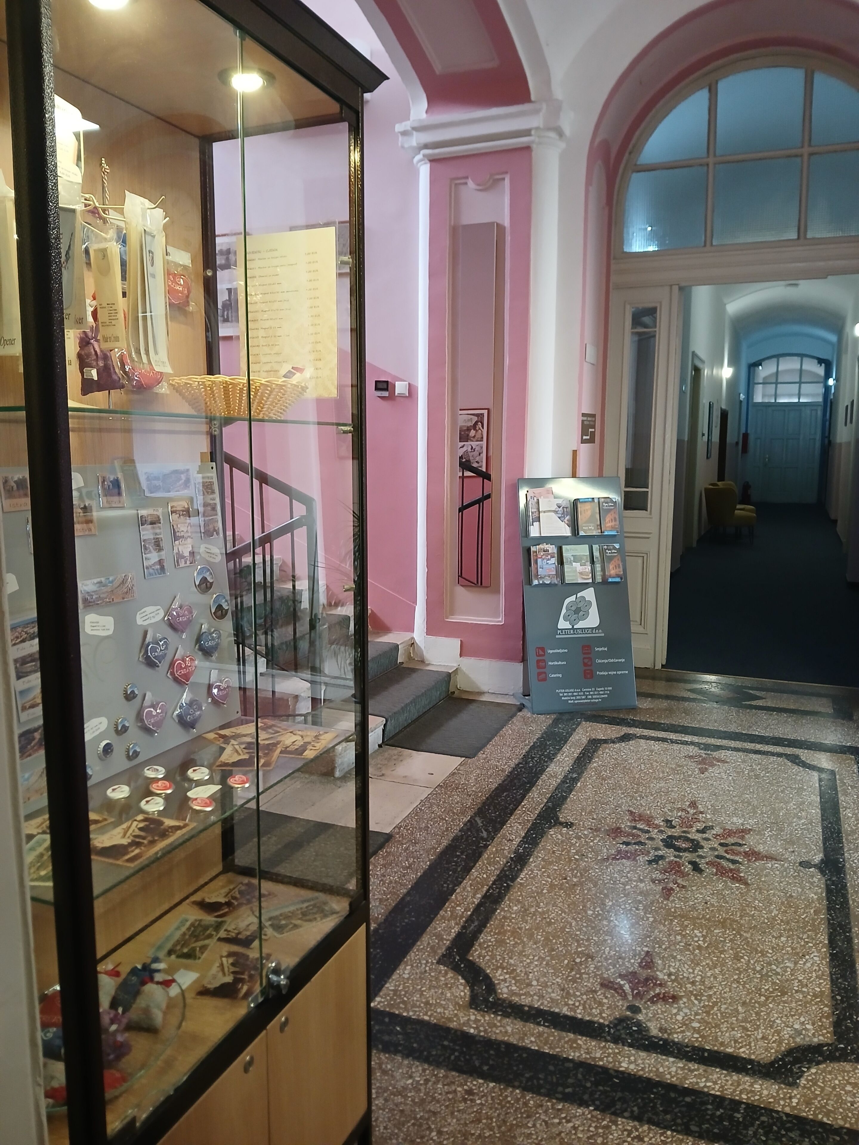 Un pasillo con un expositor de vidrio que contiene varios objetos, un mostrador de recepción y una puerta que da a otra zona.