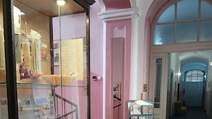 A hallway with a glass display case containing various items, a reception desk, and a door leading to another area. - Hostel veli jože (Pula)