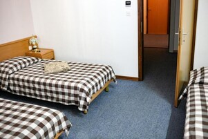 Habitación de hotel con edredón a cuadros, una mesita de noche con lámpara y una puerta que da a otra habitación.