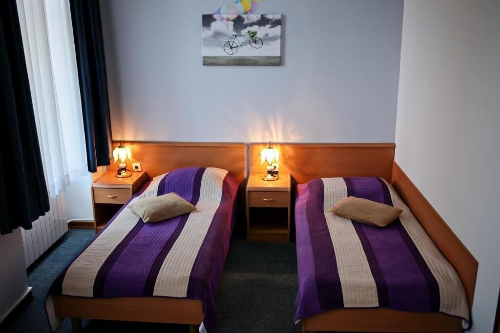 A hotel room with two single beds, each with a headboard, bedside tables, and lamps.