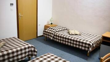 Una habitación con dos camas individuales, una puerta de madera, una mesita con una lámpara y un escritorio.