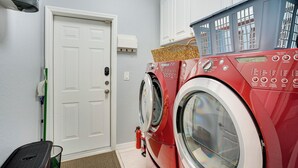 A laundry room with a red washing machine, a white door, and a green broom. - Heated Pool & Lanai Cookouts! Cape Coral Getaway (Cape Coral)