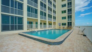 Ein Hotelpool mit gefliestem Sonnendeck, einem Pool und einem Gebäude mit mehreren Balkonen.