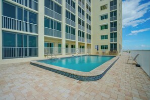 A hotel pool area with a tiled deck, a pool, and a building with multiple balconies. - On the Beach Condo for the Ultimate in Relaxation (Bonita Springs)
