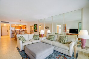 A living room with a sofa set, ottoman, and a large mirror. There is a dining area in the background with wooden furniture. - On the Beach Condo for the Ultimate in Relaxation (Bonita Springs)