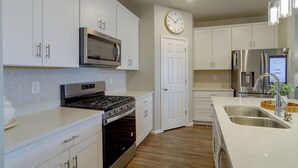 A modern kitchen with white cabinetry, stainless steel appliances, a microwave, oven, and a clock on the wall. - Private Yard w/ Patio! Modern Commerce City Gem (Commerce City)