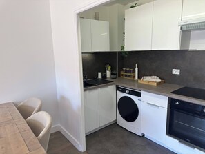 Een functionele keuken met witte kastjes, een vaatwasser, een oven en een eethoek met een houten tafel en stoelen.