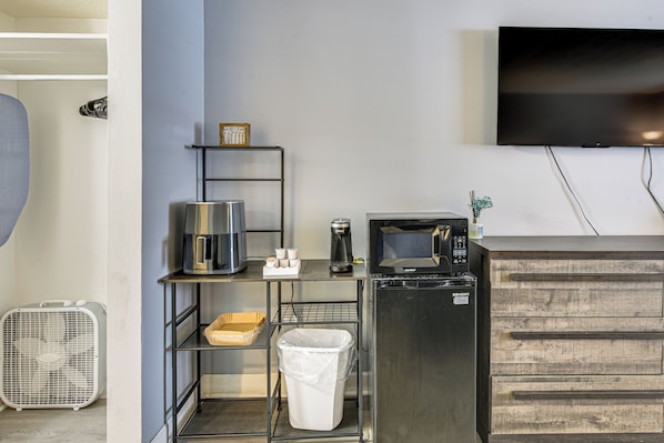 Una kitchenette compacta con cafetera, microondas y un pequeño estante con una taza de café.