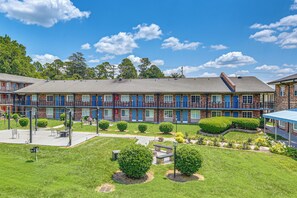 A multi-story hotel with a brick facade, balconies, and a well-maintained lawn with shrubs. - Work & Play! Studio Near Uptown, Hospitals, Sports (Charlotte)