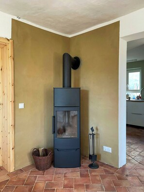 A corner room with a black wood-burning stove, a wicker basket, and a tiled floor. - Quiet studio retreat with a peaceful garden (Wenzlow OT Boecke)