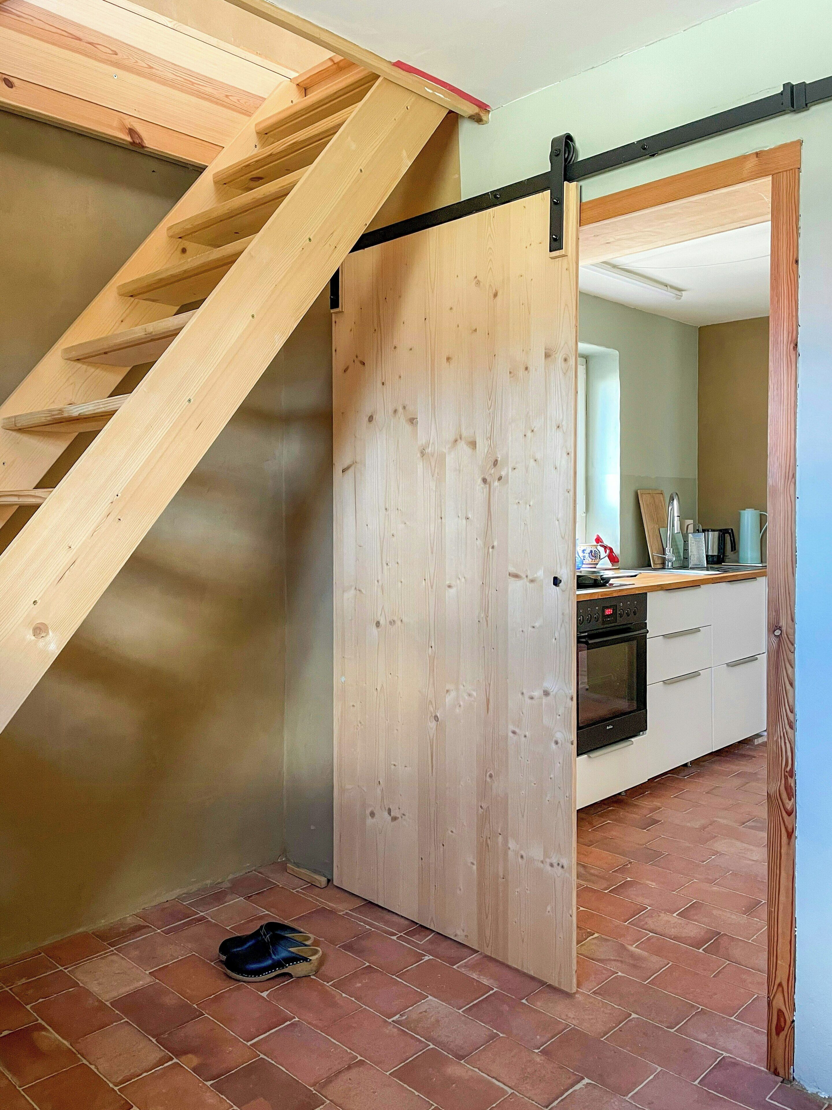 Una cucina con una scala in legno, una porta scorrevole e un pavimento piastrellato.