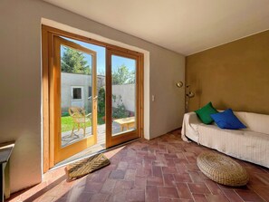 A room with a sliding glass door leading to a patio, a white sofa with blue and green cushions, and a woven pouf on the floor. - Quiet studio retreat with a peaceful garden (Wenzlow OT Boecke)