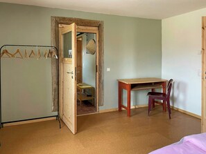 A room with a wooden desk, a chair, a coat rack, and a door leading to another room. - Quiet studio retreat with a peaceful garden (Wenzlow OT Boecke)