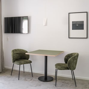 Una habitación con una mesa redonda y dos sillas, un televisor de pantalla plana montado en la pared, y un cuadro enmarcado.