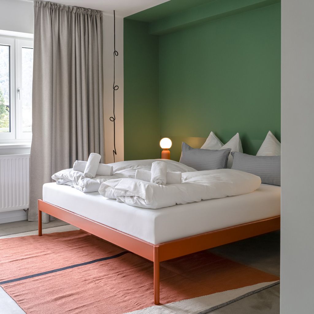 A bed with white bedding, a green wall, and a window with curtains.