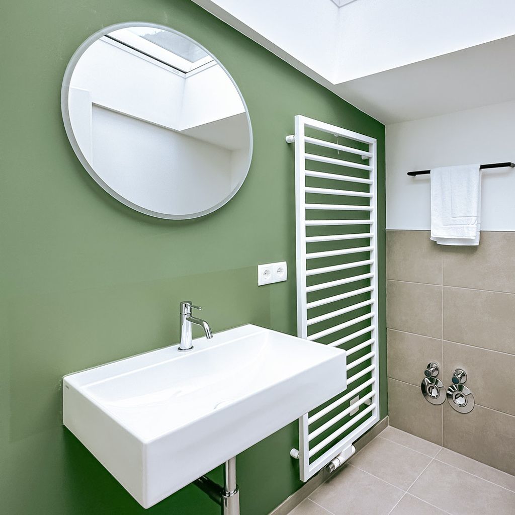 Een badkamer met een witte wasbak, een ronde spiegel, een witte handdoekhouder en een handdoek eraan.