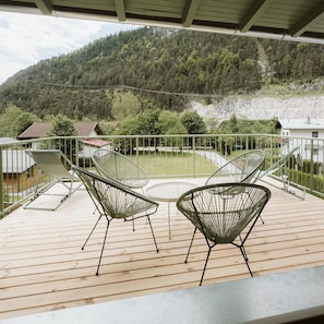 Una terraza de madera con dos sillas de metal y una mesa, con vistas a una ladera boscosa.