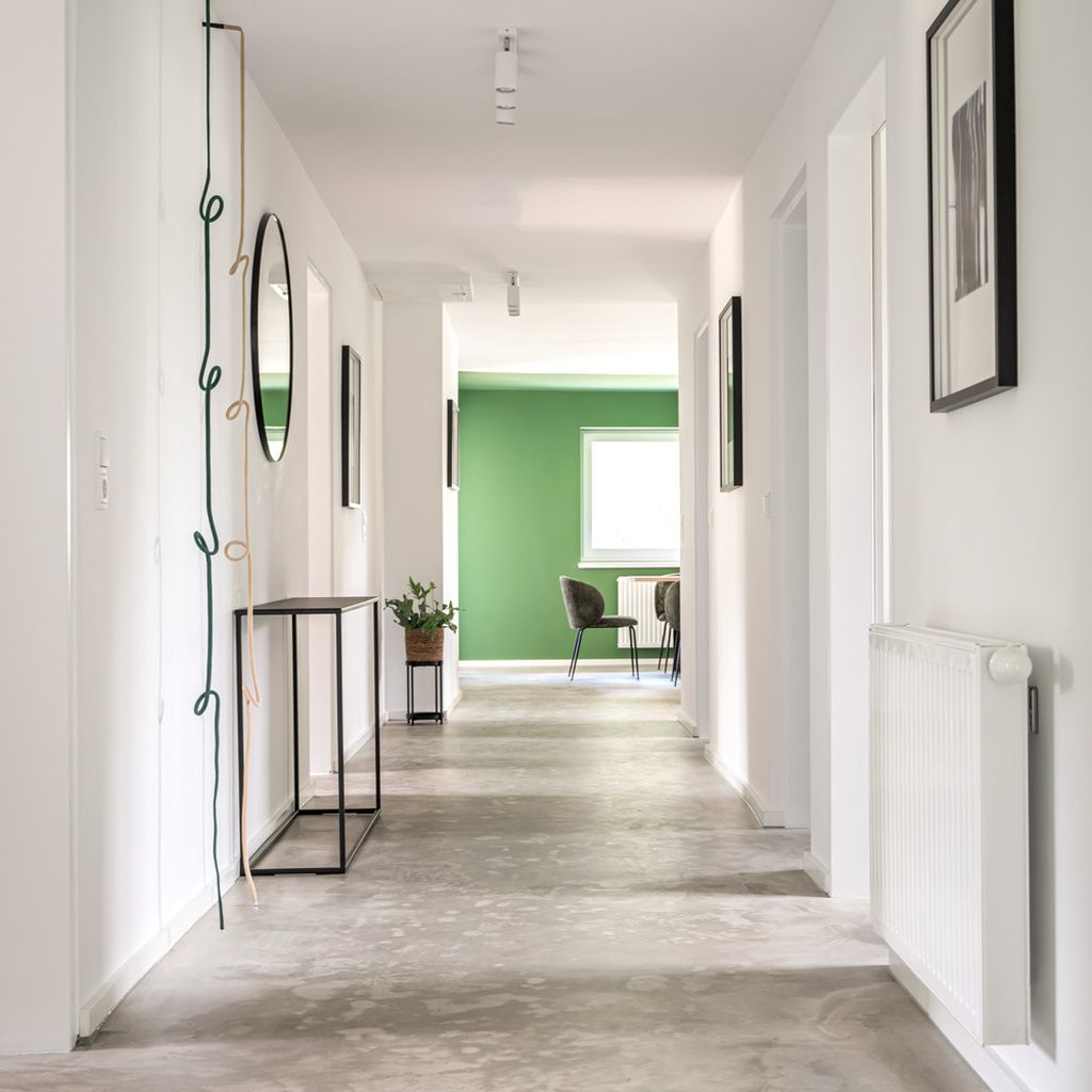 A hallway with a green wall, a radiator, and framed pictures on the walls.
