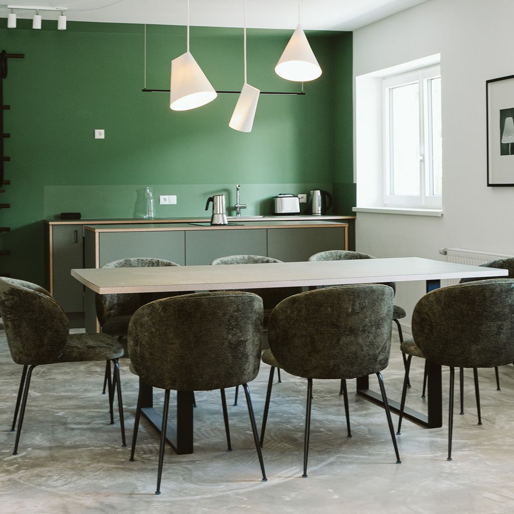 A dining area with a table and chairs, a kitchen in the background, and pendant lighting.