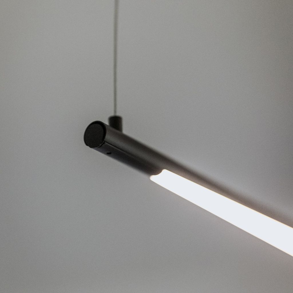 Un luminaire moderne doté d’un socle cylindrique et d’un tube lumineux droit et allongé.
