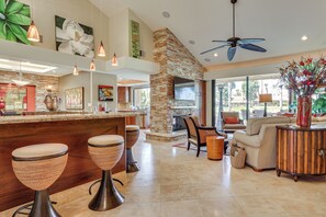 A spacious living area with a stone fireplace, a bar with stools, and a comfortable seating area with a sofa and armchairs. - Extended Getaway in the Heart of Palm Desert (Palm Desert)
